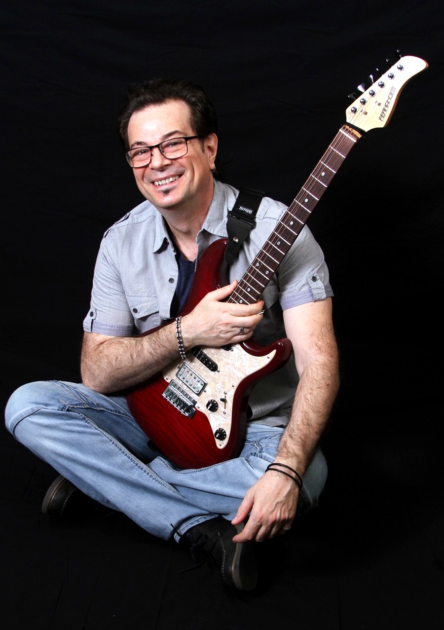 Gio Lombardi smiling with a red electric guitar